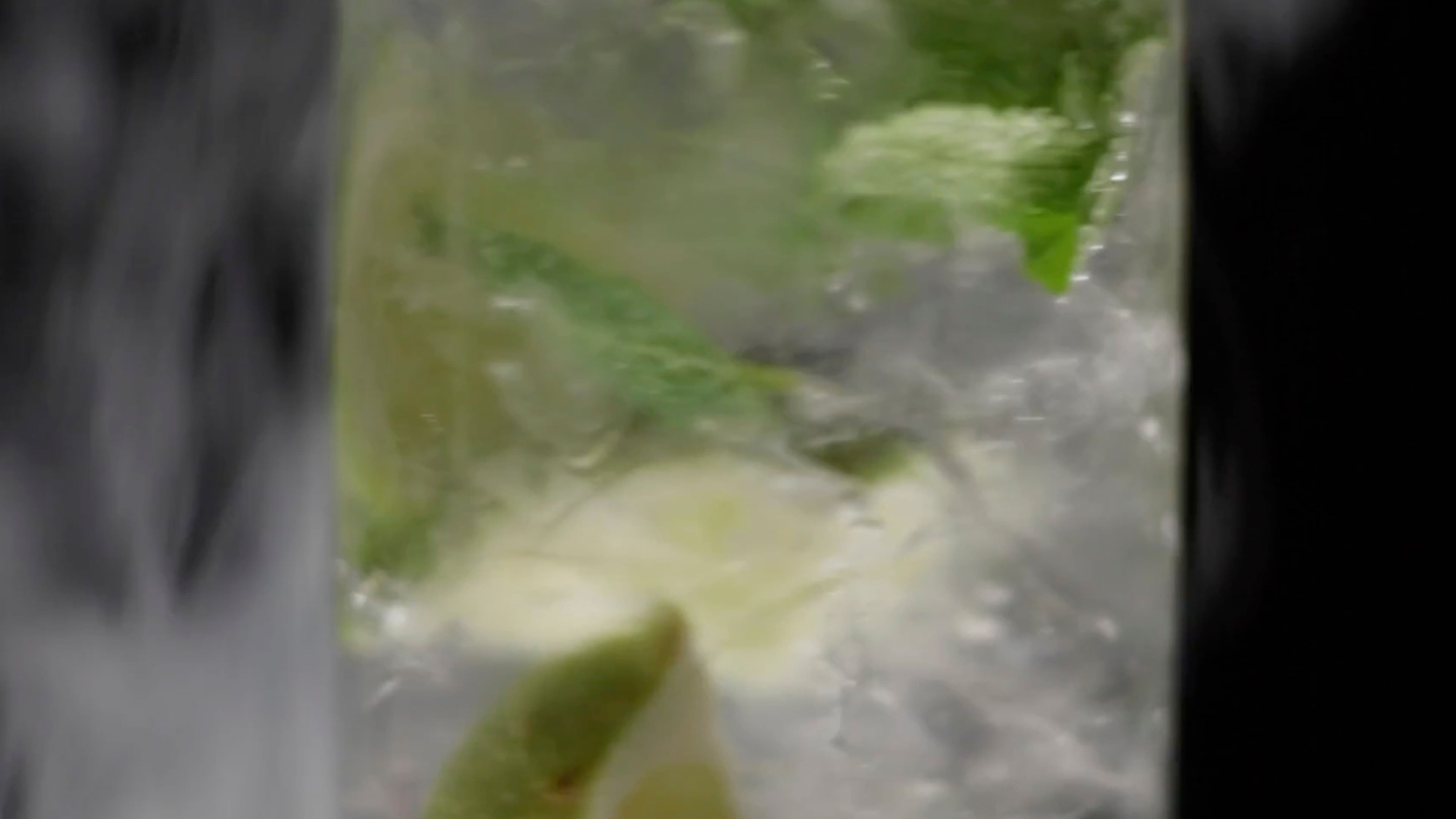 A close-up of a mojito-style cocktail glass filled with crushed ice, fresh mint, and a lime wedge.