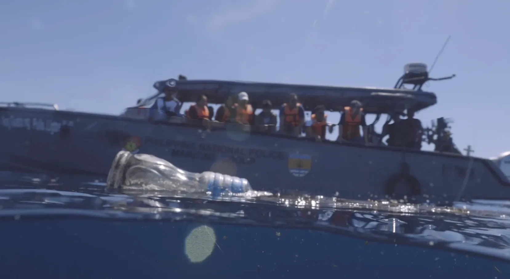 A Philippine National Police Maritime patrol boat with officers aboard, with a plastic bottle floating in the foreground.