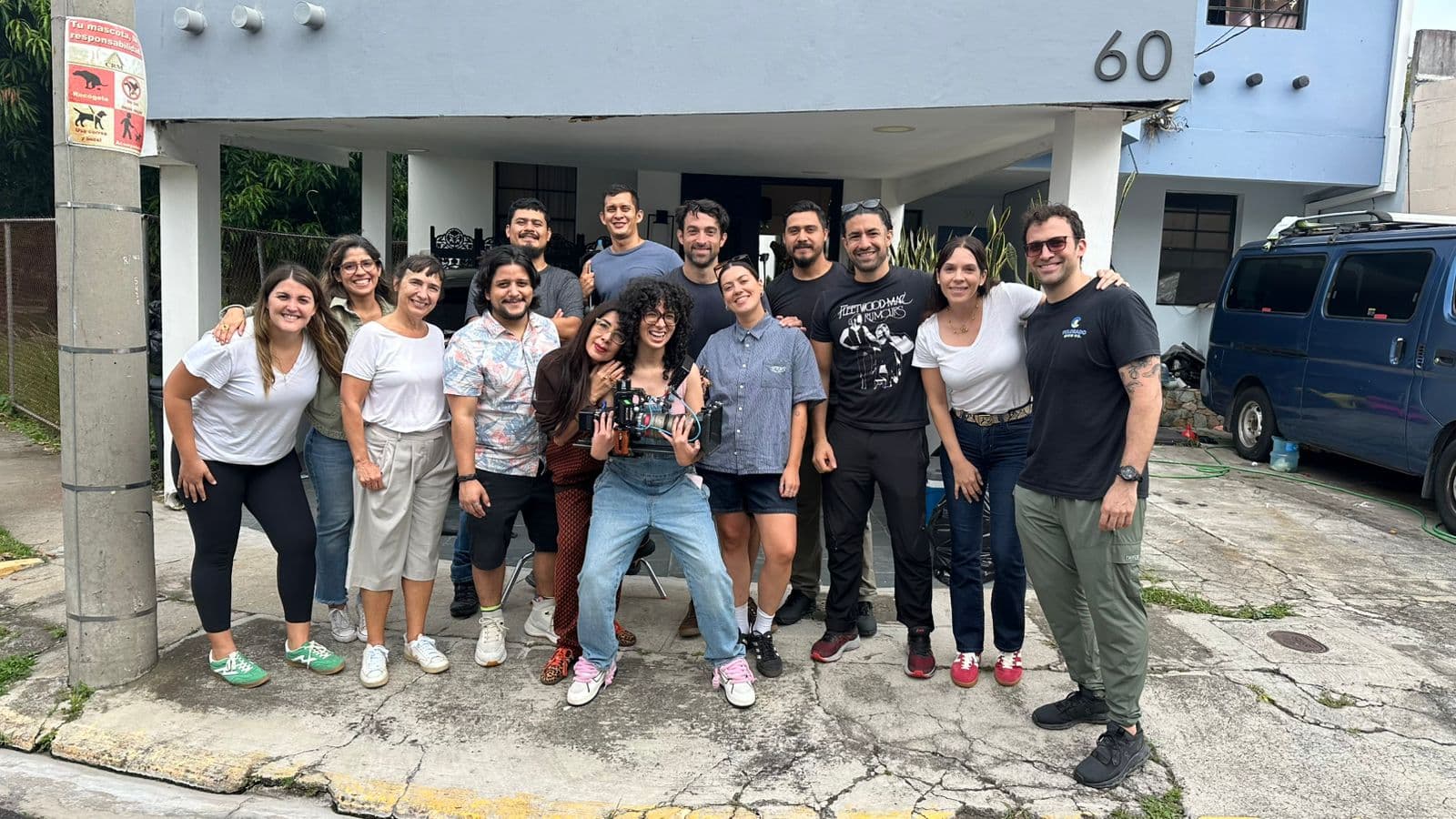 The full production crew poses together outside a house on a residential street after a day of filming.